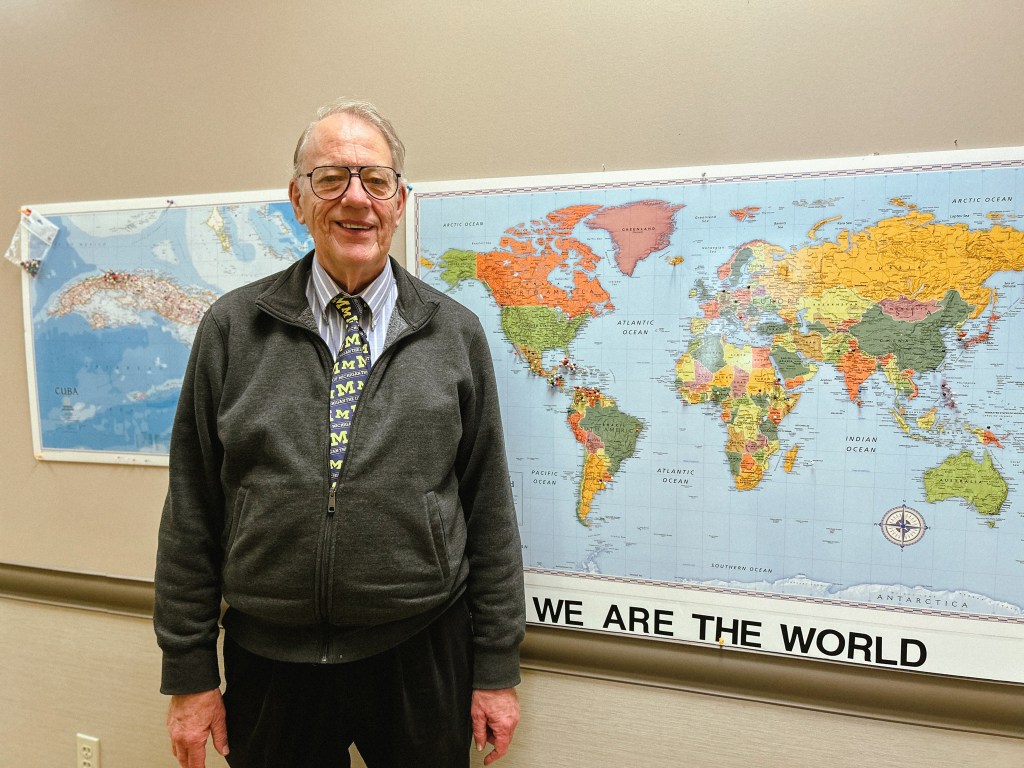Man smiling next to a map of the world